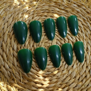 Glossy deep green almond-shaped press-on nails displayed on a natural woven mat