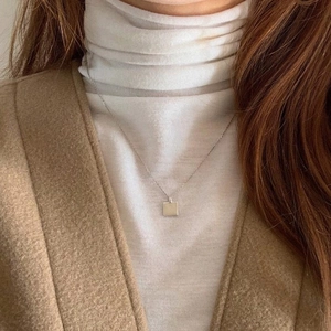 Close-up of a minimalist silver square pendant necklace worn over a white turtleneck top