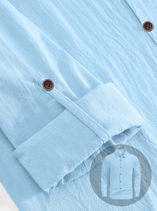 Close-up of light blue linen shirt texture with dark brown wood buttons and clean stitching