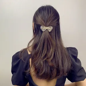 Elegant bow hair clip with white pearls on dark brown wavy hair, golden metal frame