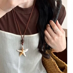 Close-up of a realistic starfish pendant on a brown cord necklace worn by a model