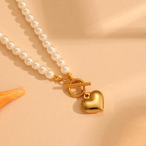 Detail of gold heart pendant pearl necklace with T-bar toggle clasp on shell background