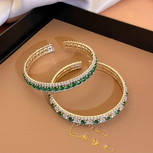 Detailed shot of gold-plated open bracelets with emerald green and white cubic zirconia