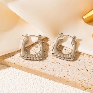 Detailed macro shot of silver geometric earrings with pleated texture on silk fabric