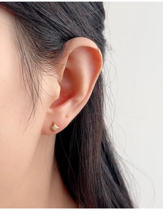 Detailed close-up of a tiny gold star stud earring with a central zircon on ear lobe