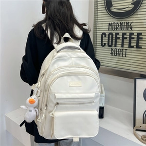 Dettaglio dello zaino bianco minimalista con tasche multiple e ciondolo a papera