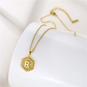 Detailed macro view of a golden hexagonal pendant necklace featuring the engraved letter R