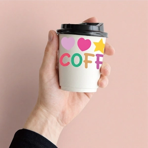 Cartoon alphabet stickers on white coffee cup with black lid held against pink background