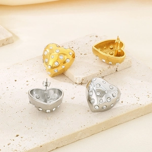 Détail de boucles d'oreilles cœur dorées et argentées avec cristaux sur pierre