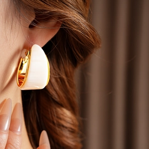 Close-up of gold plated resin hoop earring worn by a model in a minimalist style