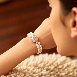 Detailed view of triple-layer pearl bracelet with pink square gemstone buckle on wrist