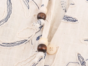 Detail of embroidered neckline with linen texture, blue stitching and wooden beads