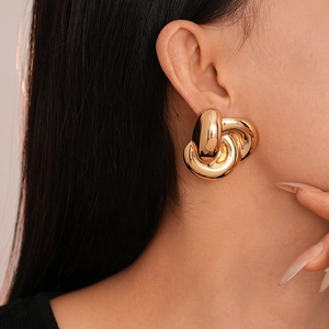 Close-up of a model wearing chunky gold knotted metal stud earrings with mirror finish