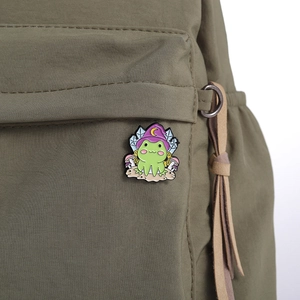 Cute magic frog enamel pin with wizard hat pinned on an olive green canvas backpack
