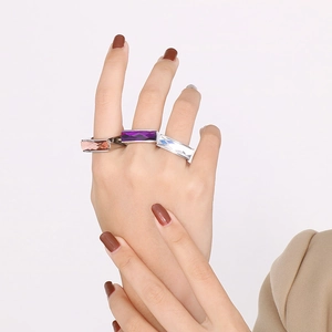 Detailed view of square glass gemstone rings in purple, pink, and clear on model's hand