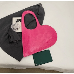 Detail of pink heart-shaped bag featuring glossy crocodile texture on a stylish flat lay