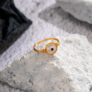 Macro view of handmade gold wire-wrapped ring with opal evil eye charm on grey stone
