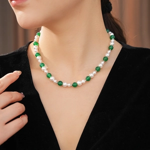 Dettaglio di una collana vintage con perle bianche e agata verde indossata da una modella