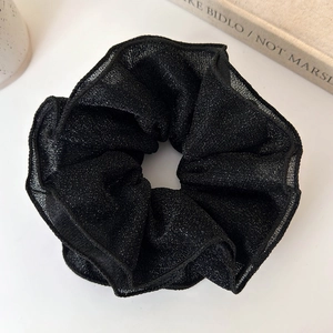 Close-up of black shimmering fabric hair scrunchie with layered lace edges on white desk