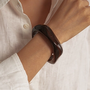 Détail d'un bracelet en acrylique ambre torsadé au poignet avec une chemise en lin