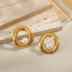 Detail view of elegant gold pearl stud earrings on a textured stone aesthetic background