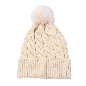 Close-up of beige cable knit beanie featuring thick texture and a fluffy faux fur pompom