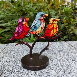 Close-up of three colorful stained glass birds perched on a bronze branch base