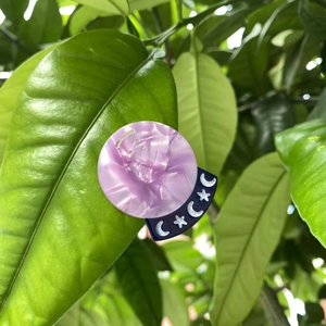Detail of purple marble acetate hair clip with blue moon and star symbols on green leaves