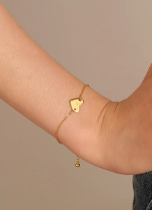 Détail d'un bracelet doré avec pendentif en cœur et lettre P gravée au style minimal