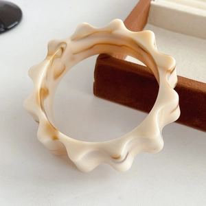 Detail of cream wavy resin bangle with brown amber texture and polished finish