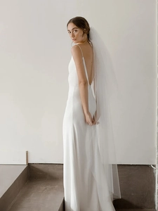 Detail of a minimalist white backless bridal gown with a floor-length sheer tulle veil