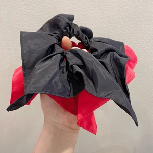 Close-up of black and red plaid bow scrunchie with satin texture held in hand