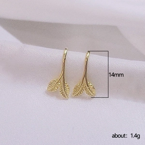 Leaf shaped gold studs with detailed vein textures on white fabric background