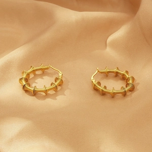 Detailed close-up of golden spiral hoop earrings on champagne silk background