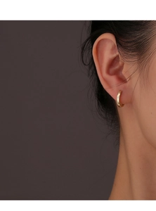 Gros plan de boucles d'oreilles huggies dorées avec zircons portées par un modèle