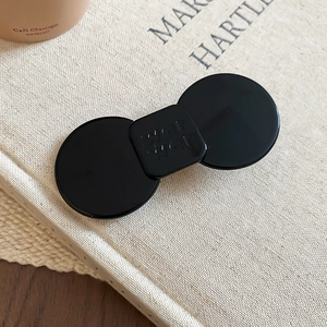 Detail view of a black resin hair clip with engraved letters on a textured book surface