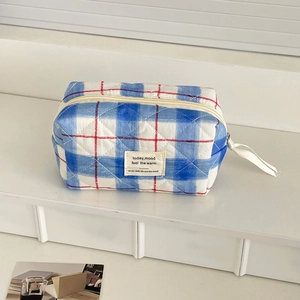 Close-up of a blue and white checkered quilted makeup bag with a red zipper accent