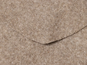 Macro detail of soft beige knitted fabric texture showing premium edge stitching quality