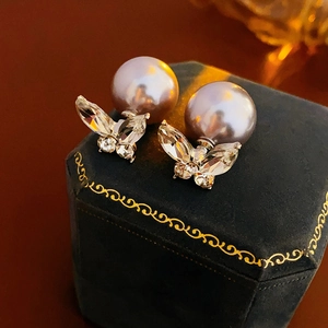 Détail de boucles d'oreilles papillon en zircon et perles sur écrin en velours bleu