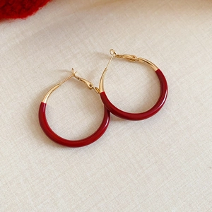Macro shot of gold hoop earrings with red enamel finish on beige fabric texture