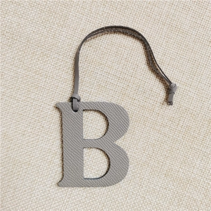 Macro view of grey textured leather letter B keychain accessory on woven background