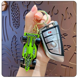 Detailed close-up of a green cartoon racing car keychain held with a car key remote