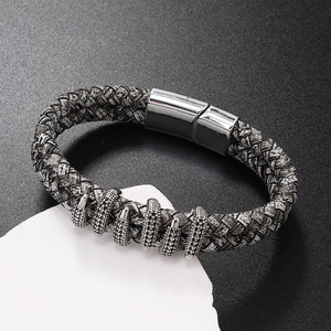 Detailed view of woven leather bracelet with silver spikes and black stones on white stone