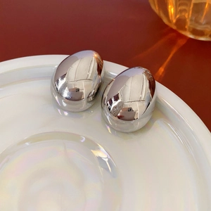 Close-up of silver oval stud earrings with polished mirror finish on white plate