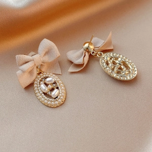 Macro shot of vintage bow pearl earrings with rhinestones on champagne silk fabric