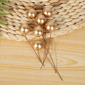 Vue détaillée de 7 baies décoratives dorées avec tiges sur une surface de table en bois