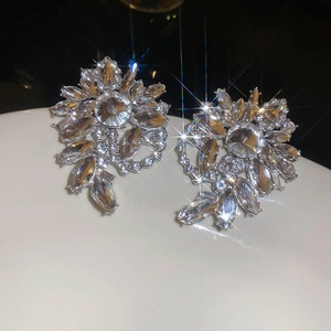 Close-up of oversized silver flower earrings with sparkling crystals on a black background