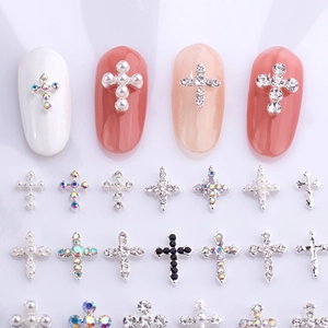 Dettaglio di ciondoli a croce per nail art con strass e perle su sfondo viola chiaro