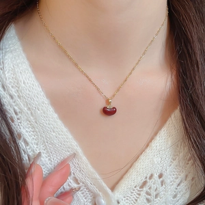 Close-up of gold necklace with a deep red heart pendant and tiny diamonds on a model