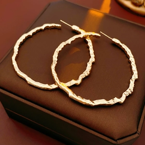 Détail de créoles dorées texturées posées sur un écrin à bijoux marron chic